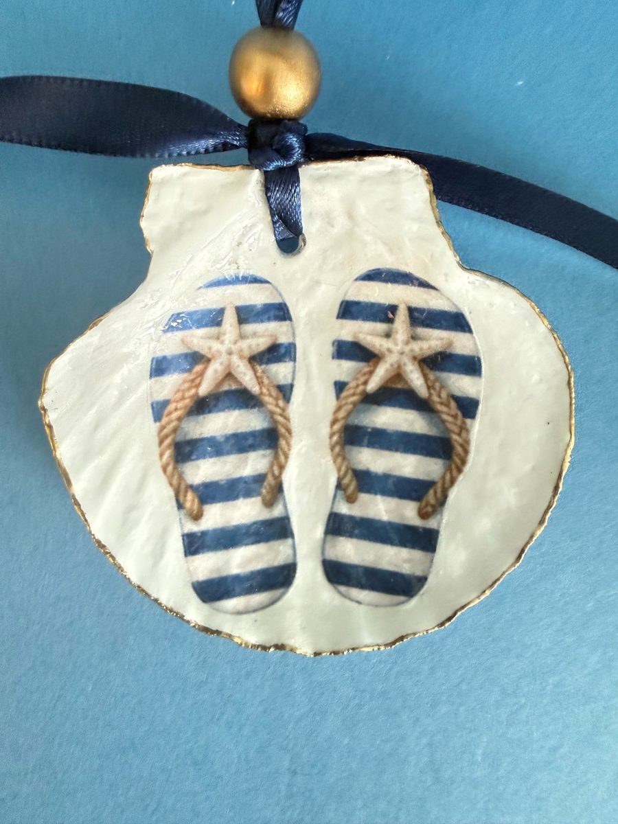 Gold-edged scallop shell with navy-striped flip-flops topped with starfish, hung on a navy ribbon with a gold bead